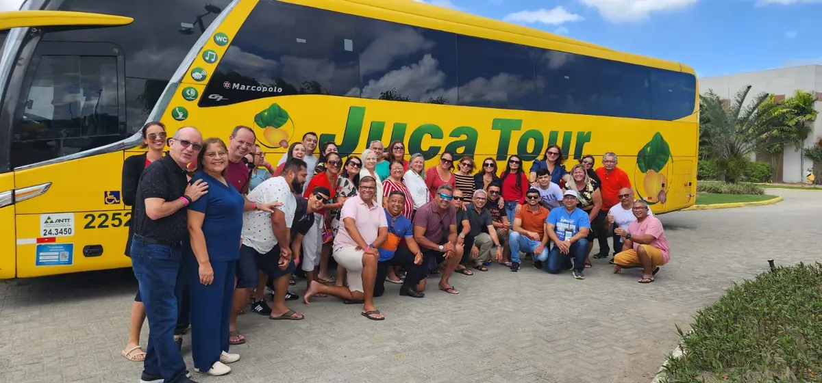 Turma de mais de 40 clientes reunida na frente do ônibus da excursão